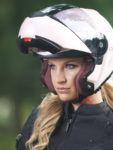 A blonde haired female motorcyclist wearing a white modular style helmet with the chinbar up.