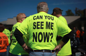 Man wearing safety green tee shirt from behind. Text on shirt reads " Can You See Me Now?"